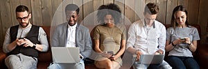 Five diverse businesspeople girls guys sitting on couch using gadgets