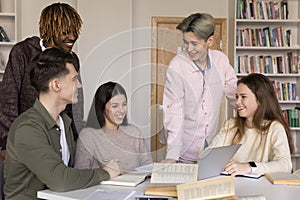 Five diverse teenage students engaged in teamwork gather in library