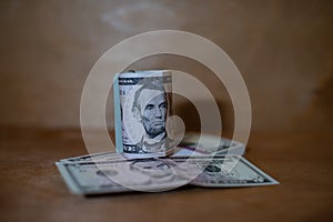 Five dollar bills in a roll lying on a bundle of banknotes.