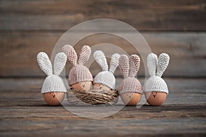 Five Easter eggs in crocheted hats with rabbit ears on a rustic wooden table.