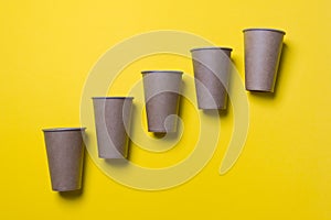 Five eco-friendly cardboard cups lie on diagonal on a yellow color paper background. Mock-up. Close-up