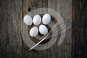 Five Eggs and Whisk or Egg Beater on Rustic Wood