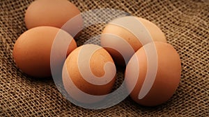 Five fresh brown chicken eggs rotating on burlap background