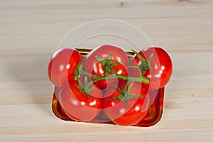 Five fresh red tomatoes with green stem in the tray , isolated on the background