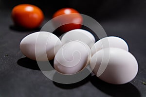 Five fresh white eggs and tomatoes on black surface