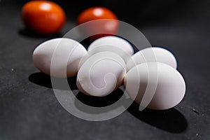 Five fresh white eggs and tomatoes on black surface