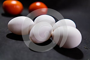 Five fresh white eggs and tomatoes on black surface