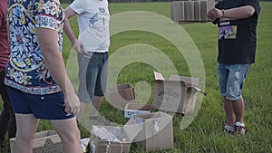 Five friends begin to collect homemade rocket from a pile of cardboard boxes in the field in the evening.
