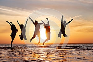 Five friends having fun and jumping at sunset beach
