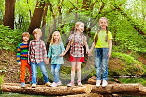 Five friends standing holding hands on log bridge