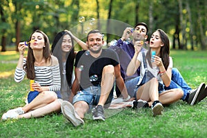 Five friends women and men inflate soap bubble outdoors