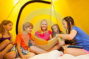 Five funny kids read book in a tent