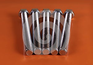 Five galvanized screws with thread next to each other on a red background.