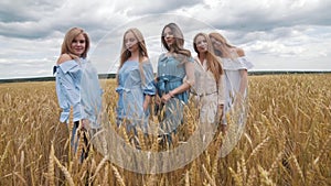 Five girls with long blond hair in a field of golden wheat. Smiling, looking at the camera.