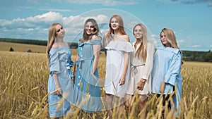 Five girls with long blond hair in a field of golden wheat. Smiling, looking at the camera.