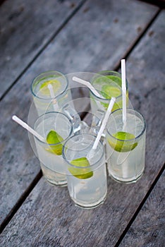 Five glasses of lemonade on a rough wooden table. Cocktails with gin, tonic and lime on a rough wooden background.