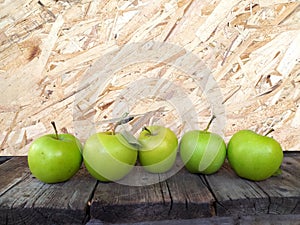 Five green apples in a row on a textured wooden table