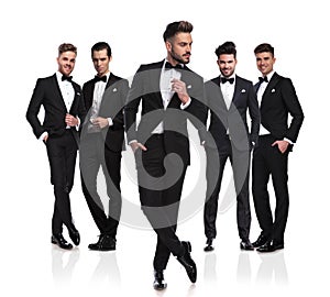 Five grooms in black tuxedoes with pensive leader in front photo