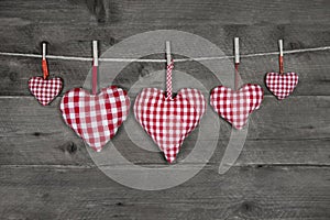 Five handmade red checkered hearts on wooden grey background.