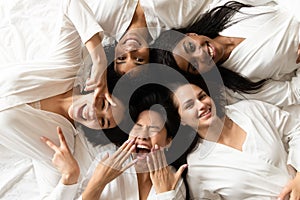 Five happy diverse young girls lying on bed, top view photo