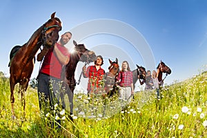 Five happy equestrians walking with their horses