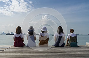 Five happy girls sit on wooden pier looking to the sea on the vacations concept