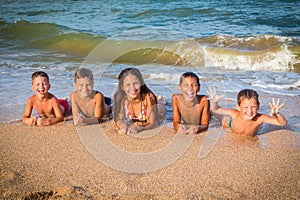 Five happy kids lying down together on the beach