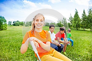 Five happy kids sit on chairs in row outdoors