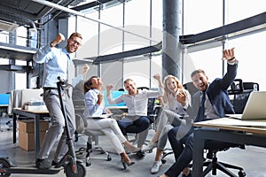 Five happy modern business people are keeping arms raised and expressing joyful while sitting in large office.