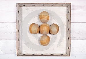 Five kiwis placed in the middle in an old wooden tray on a background of old wooden floor