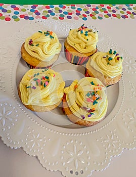 Five lemon cupcakes with yellow frosting with sprinkles on white plate