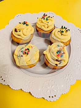 Five lemon cupcakes with yellow frosting with sprinkles on white plate