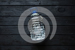 A five-liter plastic water bottle lies on a black wooden board