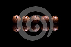 Five macadamia nuts on black reflective background