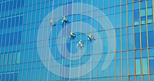 Five men workers in red and yellow work clothes cleaning the exterior windows of a business skyscraper - industrial