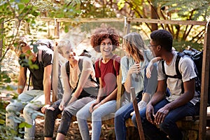 Five millennial friends sitting on a bridge in a forest talking during a hike, three quarter length photo