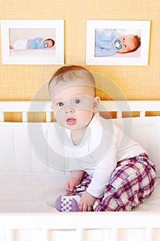 Five-months baby sits in white bed