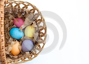 Five multi-colored eggs on straw in a wicker basket isolated on white background. Top view