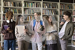 Five multi ethnic schoolmates standing in library and talking