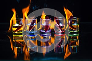 Five multicolored shot glasses full of drink and with the red ch