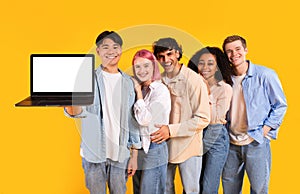 Five multiracial friends holding laptop showing blank computer screen, recommending educational website, mockup