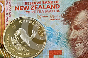 A five New Zealand dollar bill with a South African gold Krugerrand coin