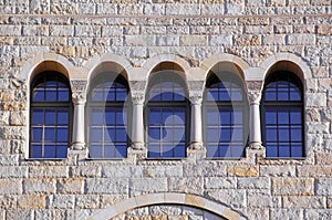 Five old windows with arches, columns and lattices on a stone wa