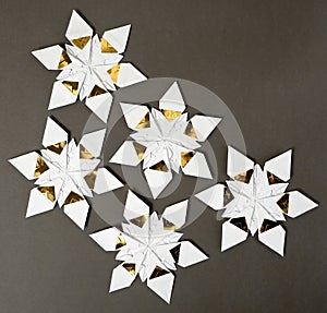 Five origami star snowflakes in white and gold foil paper, on a dark grey paper background