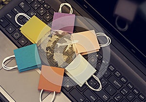Five paper shopping bags put in circle around a clear crystal globe with world map on a computer notebook keyboard. International