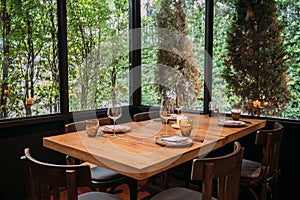 Five people dinner table with plates, knives, forks, wine glasses, glasses and napkins on wooden table with Pines and green.