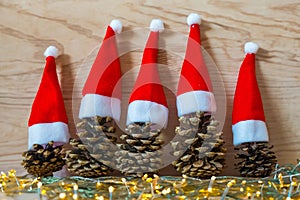 Five pine cones in a red Santa hats like a Christmas tree on a wooden background