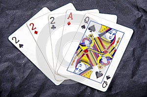 Five playing card`s a hand of a three of a kind two`s and a ace and a queen