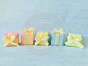 Five rainbow gradient colors square gift boxes randomly arranged in a row on a blue-green watercolor textured background.