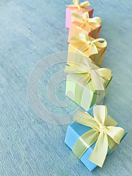 Five rainbow gradient colors square gift boxes arranged in a diagonal row on a blue-green watercolor textured background, vertical